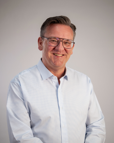 Portrait of a smiling middle-aged man wearing a light blue dress shirt against a neutral background.