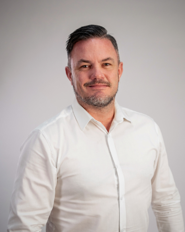 Professional head-and-shoulders portrait of a man in a white shirt, facing the camera in a neutral studio.